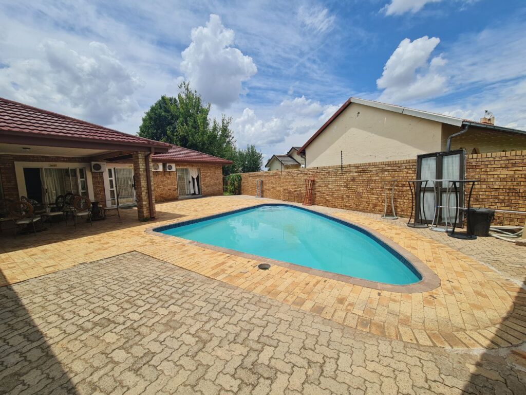 Sparkling outdoor pool at Quereba Bed and Breakfast Mafikeng with garden background and blue sky reflection.